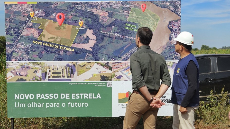 O governador Eduardo Leite (à esquerda, de camisa verde) observa um grande painel com o mapa e o plano urbanístico do Novo Passo de Estrela, acompanhado por um técnico que usa capacete branco e colete azul com o brasão do Estado. O painel mostra o traçado do novo bairro, áreas de acesso e o slogan “Um olhar para o futuro”.
