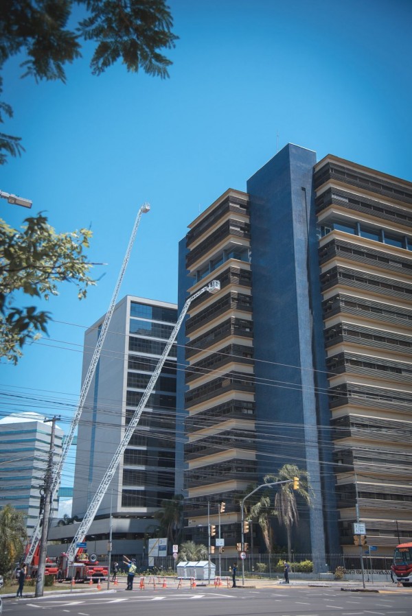 A foto duas autoescadas mecânicas de caminhões do Corpo de Bombeiros, estendidas em direção aos andares superiores de um edifício. Uma das escadas alcança quase o topo do prédio, enquanto a outra está posicionada um pouco mais abaixo. 