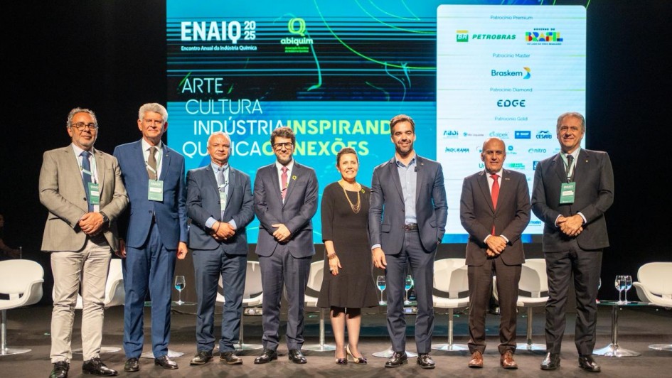 A foto mostra um grupo de oito pessoas alinhadas no palco, em frente a um painel digital com a identidade visual do evento ENAIQ 2025.