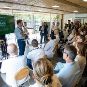 Ambiente interno com plateia atenta a uma apresentação. O governador Eduardo Leite aparece à esquerda, falando ao microfone e gesticulando enquanto apresenta os investimentos do Rio Grande do Sul durante a COP30. Ao fundo, um telão exibe o tema “Invest.RS — COP30 Brasil Amazônia”.