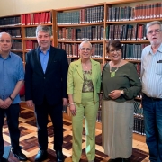 A imagem mostra cinco pessoas em pé, posando para a foto, em uma biblioteca. Ao fundo, há diversas prateleiras cheias de livros catalogados. 