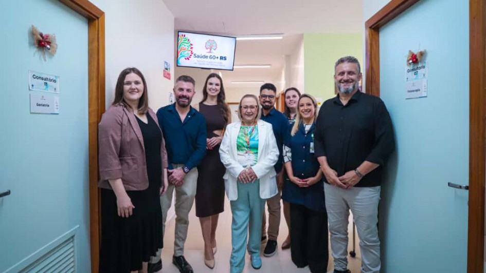 A imagem mostra um grupo de pessoas em pé, posando para a foto em um corredor de um centro médico. A secretária da Saúde está ao centro. 