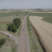 Foto de uma estrada de mão dupla reta, com curvas mais à frente, no meio de área rural.