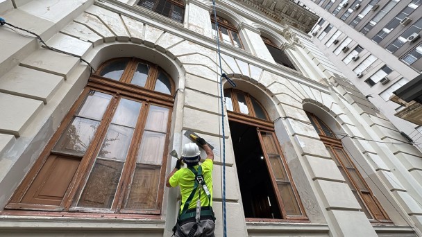 Foto mostra operário trabalhando no restauro da parede externa do Colégio Paula Soares, em Porto Alegre