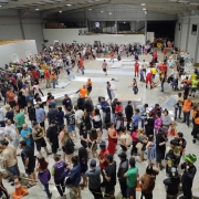 Imagem mostra um grande salão com muitas filas de pessoas aguardando serem atendidas. Auxiliares da Defesa Civil com coletas laranjas auxiliam em diversos pontos do salão.