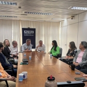 Foto mostra reunião na sala da Fgtas, com pessoas sentadas a volta de uma mesa de trabalho. O banner da Fgtas está atrás dos secretários.