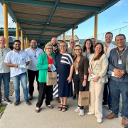 Foto posada de 14 pessoas ao ar livre, de pé, em ambiente escolar aberto, num pátio. A maioria sorri para a câmera.