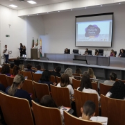 Foto de auditório, tirada meio de lado, mais para o fundo, enquadrando o palco.