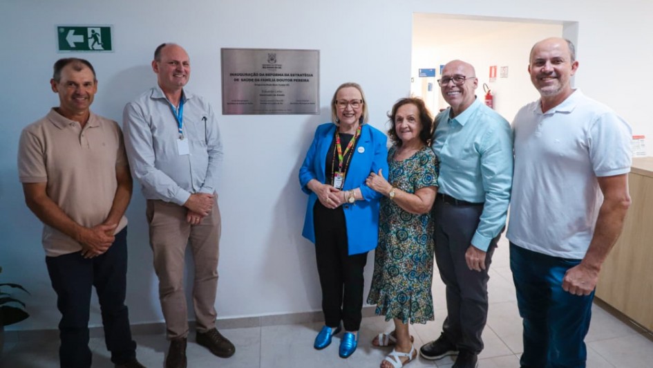 Uma foto de um homem em pé, no centro, em um palco de conferência, falando em um microfone. Ele veste um blazer escuro sobre uma camisa social branca, calças cáqui e tênis brancos. Ele gesticula com a mão direita em direção a uma grande tela de projeção atrás dele.

A tela exibe o título "RIO GRANDE DO SUL DO FUTURO" em letras grandes, com um subtítulo que menciona "TRANSFORMAÇÃO, RECONSTRUÇÃO E DESENVOLVIMENTO". O fundo do slide é uma imagem aérea de uma cidade costeira (Porto Alegre, provavelmente) ao pôr do sol.

No fundo, na parede, o nome "AMCHAM" está em letras grandes e cinzas. A plateia, composta por diversas pessoas, está sentada em fileiras em primeiro plano, com o foco desfocado.