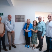 Uma foto de um homem em pé, no centro, em um palco de conferência, falando em um microfone. Ele veste um blazer escuro sobre uma camisa social branca, calças cáqui e tênis brancos. Ele gesticula com a mão direita em direção a uma grande tela de projeção atrás dele.

A tela exibe o título "RIO GRANDE DO SUL DO FUTURO" em letras grandes, com um subtítulo que menciona "TRANSFORMAÇÃO, RECONSTRUÇÃO E DESENVOLVIMENTO". O fundo do slide é uma imagem aérea de uma cidade costeira (Porto Alegre, provavelmente) ao pôr do sol.

No fundo, na parede, o nome "AMCHAM" está em letras grandes e cinzas. A plateia, composta por diversas pessoas, está sentada em fileiras em primeiro plano, com o foco desfocado.