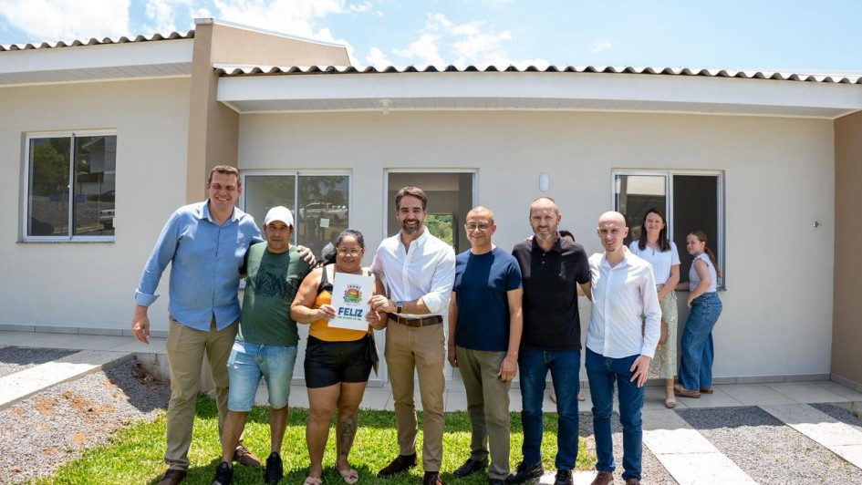 Foto mostra o governador Eduardo Leite, ao centro, entre grupo de pessoas, durante cerimônia para entrega de moradias em Feliz