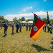 Foto mostra solenidade de formatura com policiais militares conduzindo as bandeiras do Estado e do Brasil