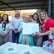 Foto mostra secretária Arita Bergmann, ao centro, segurando contrato, com duas pessoas na sua direita e outras duas pessoas à esquerda
