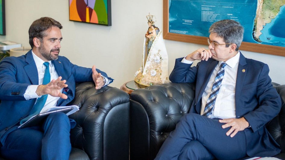 Foto de Leite e Randolfe sentados num sofá em uma sala, ambos voltados um para o outro, conversando. Leite fala e gesticula com a mão direita.