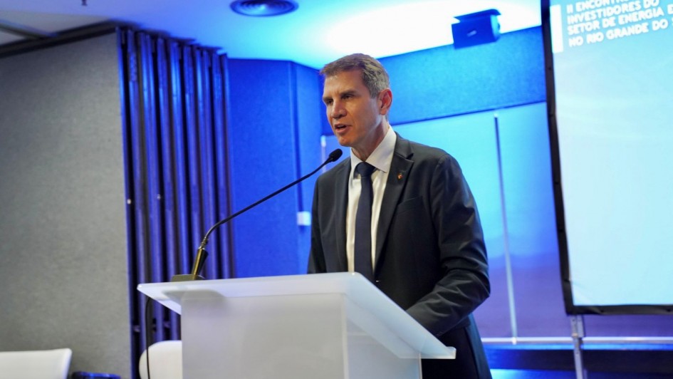 Foto de Polo falando ao púlpito, em ambiente fechado. Ao fundo há uma projeção de slide de cor azul. 