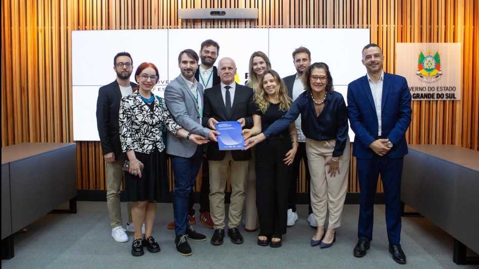 Um grupo de dez pessoas posa para foto com um documento em mãos em um ambient de uma sala formal.