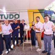 Foto externa mostrando um grupo de pessoas em pé diante de um veículo grande adesivado com as cores verde, amarela e vermelha e os dizeres “TUDO FÁCIL”. No centro, há um cavalete com placa inaugurada. Todos aplaudem, entre eles o governador Eduardo Leite.