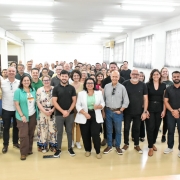 Foto posada em sala fechada, com mais de 50 pessoas de p&eacute; de frente para a c&acirc;mera. &Agrave; frente, com outras pessoas ao lado, aparece a secret&aacute;ria Marjorie, ao centro.