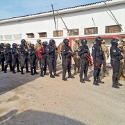 Foto mostra agentes penais enfileirados diante do muro de uma unidade prisional