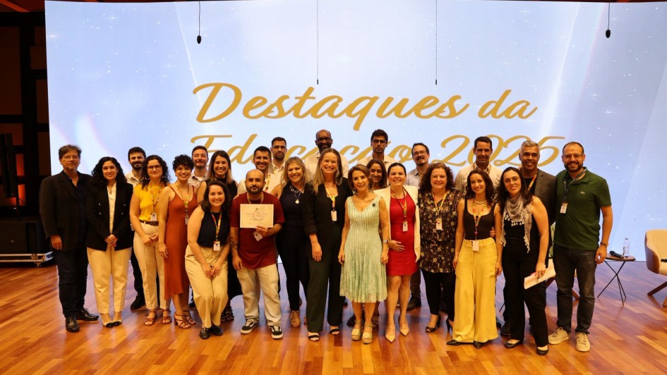 Foto mostra grupo de pessoas com certificados e posando juntas para fotos, em frente a um tel&atilde;o com a palavra "Destaques".