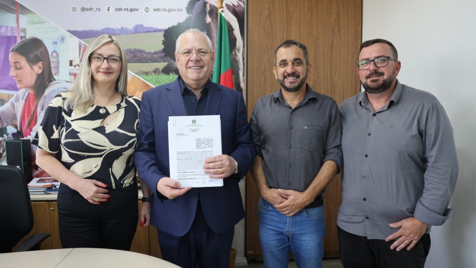 Foto mostra o secret&aacute;rio com um documento na m&atilde;o, ao lado de uma mulher e dois homens, que posam sorridentes para a foto.