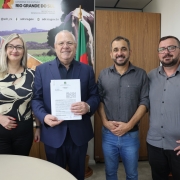 Foto mostra o secret&aacute;rio com um documento na m&atilde;o, ao lado de uma mulher e dois homens, que posam sorridentes para a foto.
