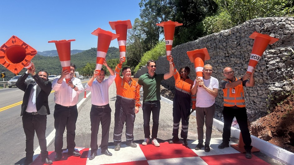 Grupo de pessoas em estrada rec&eacute;m-pintada, segurando cones de tr&acirc;nsito sobre a cabe&ccedil;a em gesto comemorativo.