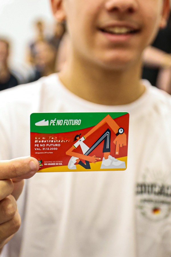 Foto mostra em primeiro plano cartão do programa, nas mãos de um estudante cuja imagem está desfocada.