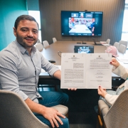 Vice governador Gabriel Souza aparece na foto ao lado da secret&aacute;ria Arita Bergmann, ambos seguram um documento, com uma tela com outros participantes online ao fundo.