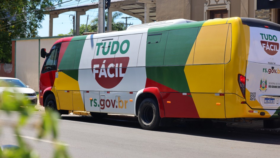Foto do ve&iacute;culo, que se assemelha a um &ocirc;nibus, estacionado na rua. O autom&oacute;vel tem as cores amarela, vermelha, verde e branca e os dizeres "Tudo F&aacute;cil - rs.gov.br" em destaque.