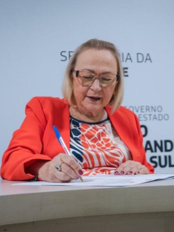 Foto mostra retrato da secretária assinando o documento.