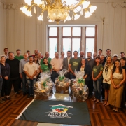 Foto posada de mais de 30 pessoas, em p&eacute; e de frente para a c&acirc;mera, num ambiente fechado e solene. &Agrave; frente, h&aacute; tr&ecirc;s cestas embrulhadas com objetos que n&atilde;o se consegue identificar.