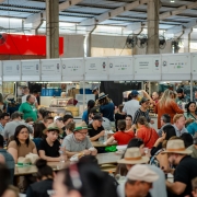 A imagem mostra o Pavilh&atilde;o da Agricultura Familiar na Expointer 2025. O local est&aacute; cheio de pessoas e h&aacute; diversas bancas de produtos variados. 