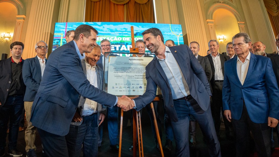 Governador Eduardo Leite e secret&aacute;rio Ernani Polo se cumprimentam cercado por outras autoridades, que os observam.