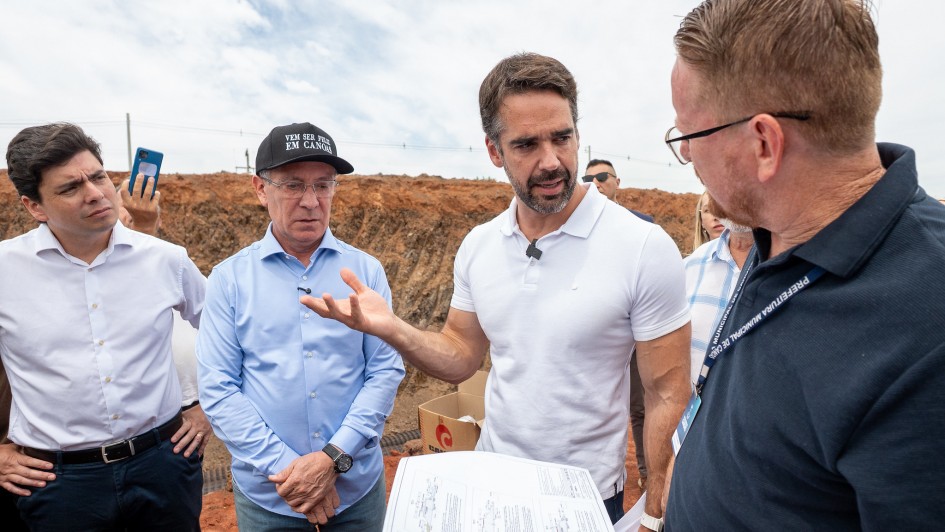 Foto ao ar livre, em ambiente de obras, com o governador gesticulando enquanto fala no centro da foto, com tr&ecirc;s homens ao redor.