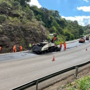 A imagem mostra uma rodovia em obras, cm máquinas e trabalhadores na pista.
