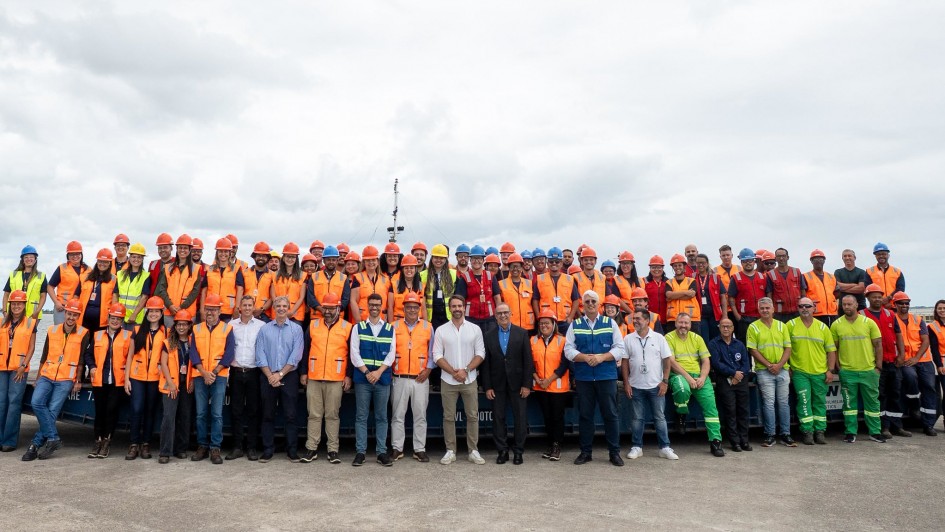 Esta &eacute; uma descri&ccedil;&atilde;o da imagem para fins de acessibilidade:

Descri&ccedil;&atilde;o da Imagem
Uma fotografia colorida em plano aberto mostra o governador Eduardo Leite posando para uma foto oficial com um grande grupo de trabalhadores e autoridades no Porto de Rio Grande, em celebra&ccedil;&atilde;o &agrave; assinatura da concess&atilde;o para o novo terminal da CMPC.

Composi&ccedil;&atilde;o: O grupo &eacute; massivo, composto por dezenas de pessoas (aproximadamente 80), organizadas em tr&ecirc;s fileiras horizontais. Eles est&atilde;o posicionados em uma &aacute;rea externa, sobre o que parece ser uma plataforma ou balsa azul.

Eduardo Leite: Localizado ao centro da primeira fila, o governador veste uma camisa social branca de mangas compridas (dobradas) e cal&ccedil;a bege clara. Ele sorri para a c&acirc;mera com as m&atilde;os cruzadas &agrave; frente do corpo.

Os Trabalhadores: A maioria dos presentes utiliza equipamentos de prote&ccedil;&atilde;o individual (EPIs). Predominam os coletes reflexivos laranjas e capacetes de prote&ccedil;&atilde;o laranjas. No canto direito, um pequeno grupo veste uniformes de alta visibilidade em verde lim&atilde;o e amarelo. Algumas pessoas usam capacetes azuis ou amarelos, indicando diferentes fun&ccedil;&otilde;es t&eacute;cnicas.

Autoridades e Convidados: Na primeira fila, ao lado do governador, encontram-se homens e mulheres em trajes sociais ou casuais-finos, al&eacute;m de alguns integrantes usando coletes azuis com logotipos institucionais.

O Ambiente: O cen&aacute;rio &eacute; portu&aacute;rio. O grupo est&aacute; em uma estrutura de concreto ou metal (balsa). Ao fundo, observa-se uma extens&atilde;o de &aacute;gua e o mastro de uma embarca&ccedil;&atilde;o que se alinha verticalmente ao centro da foto. O c&eacute;u est&aacute; completamente nublado, em tons de cinza claro e branco.