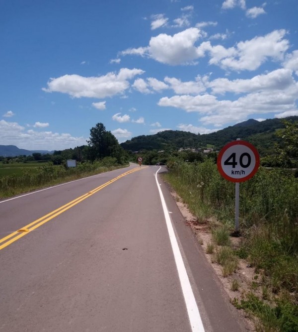 Imagem de uma rodovia asfaltada, com morros ao fundo e um céu azul com nuvens. 