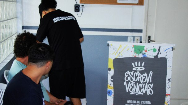 A imagem mostra tr&ecirc;s jovens de costas, sem que seja poss&iacute;vel visualizar seus rostos. No lado direito, h&aacute; um banner onde se l&ecirc; "Escreviv&ecirc;ncias - oficina de escrita criativa para jovens".