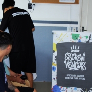 A imagem mostra tr&ecirc;s jovens de costas, sem que seja poss&iacute;vel visualizar seus rostos. No lado direito, h&aacute; um banner onde se l&ecirc; "Escreviv&ecirc;ncias - oficina de escrita criativa para jovens".