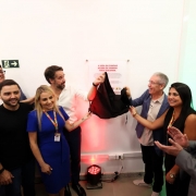 Um grupo de autoridades, incluindo o governador Eduardo Leite e o vice-governador Gabriel Souza, est&aacute; reunido para o descerramento de uma placa inaugural na parede branca. O governador segura o tecido preto que cobria a placa, revelando um texto que come&ccedil;a com a frase em destaque: "A vida em Canoas acaba de ganhar mais agilidade". As pessoas ao redor sorriem e aplaudem o momento.