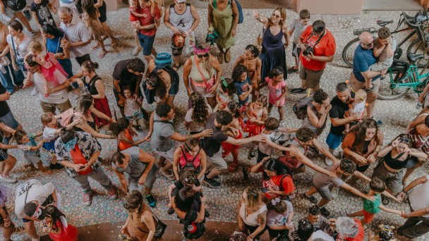 Imagem a&eacute;rea de diversas crian&ccedil;as e adultos pulando carnaval na rua. 