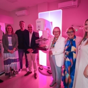 Esta &eacute; a descri&ccedil;&atilde;o detalhada da oitava imagem para fins de acessibilidade:

Imagem 8: Entrega de Mam&oacute;grafo na Santa Casa de Pelotas
A imagem retrata a cerim&ocirc;nia de entrega ou inaugura&ccedil;&atilde;o de um novo equipamento m&eacute;dico em uma sala de exames hospitalares.

Equipamento Central: No centro da imagem, destaca-se um mam&oacute;grafo moderno da marca Siemens. O aparelho &eacute; branco e possui um grande painel retangular ao fundo que emite uma luz branca intensa, iluminando a cena.

Pessoas: Um grupo de sete pessoas (quatro mulheres e tr&ecirc;s homens) est&aacute; posicionado ao redor do equipamento.

Todos est&atilde;o sorrindo para a c&acirc;mera em uma postura formal.

Uma mulher ao centro, vestindo um blazer branco e cal&ccedil;as azuis claras, estende a m&atilde;o em dire&ccedil;&atilde;o ao mam&oacute;grafo, apresentando-o.

Os demais vestem roupas casuais e sociais, incluindo blazers, vestidos coloridos e camisas polo.

Ambiente e Ilumina&ccedil;&atilde;o:

A sala &eacute; banhada por uma ilumina&ccedil;&atilde;o ambiente em tons de rosa e magenta, possivelmente em alus&atilde;o &agrave; campanha de conscientiza&ccedil;&atilde;o do Outubro Rosa.

As paredes s&atilde;o de cor clara e o teto possui dois aparelhos de ar-condicionado instalados.

Ao fundo, &agrave; direita, h&aacute; um painel el&eacute;trico com uma luz verde acesa e a indica&ccedil;&atilde;o de voltagem "220".

Clima: A imagem transmite uma sensa&ccedil;&atilde;o de conquista, celebra&ccedil;&atilde;o e avan&ccedil;o na infraestrutura de sa&uacute;de local.