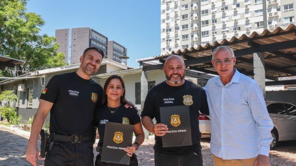 Ao centro, policiais penais Grasiele Shmaltz e Everton Muniz receberam reconhecimento pela bravura e presteza de sua conduta, das m&atilde;os de o secret&aacute;rio de Sistemas Penal e Socioeducativo, Jorge Pozzobom (D), e o superintendente da Pol&iacute;cia Penal, Sergio Dalcol (E)