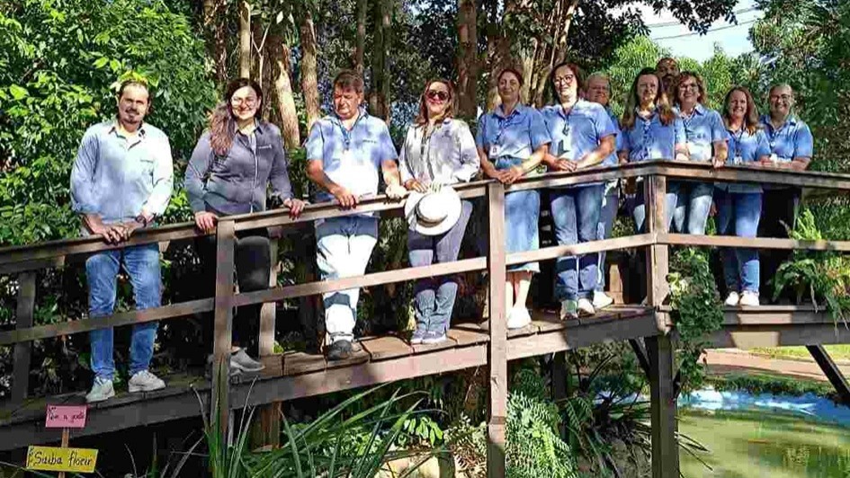 A imagem mostra um grupo de pessoas alinhadas para a foto, em p&eacute; em cima de uma ponte em meio a &aacute;rvores e plantas. 