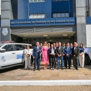 Secret&aacute;rio Ikeda e servidores do IGP posam para fotografia entre duas viaturas novas. Ao fundo, a fachada do pr&eacute;dio do IGP.