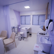 Foto mostra ambulat&oacute;rio com mesas para atendimento, maca e pias para lavaem das m&atilde;os. As paredes e m&oacute;veis s&atilde;o na tonalidade lil&aacute;s.