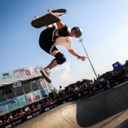 Foto mostra skatista no ar durante uma manobra em uma pista. Ao fundo o p&uacute;blico acompanha a manobra.