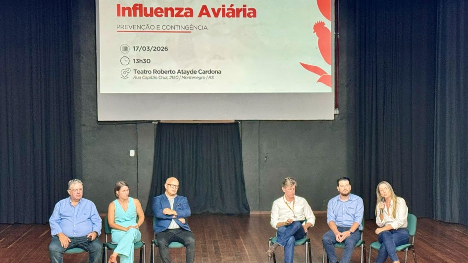 A imagem mostra um palco de audit&oacute;rio onde seis pessoas est&atilde;o sentadas em cadeiras alinhadas. Acima delas, um grande tel&atilde;o exibe o t&iacute;tulo &ldquo;2&ordm; F&oacute;rum Estadual de Influenza Avi&aacute;ria &ndash; Preven&ccedil;&atilde;o e Conting&ecirc;ncia&rdquo;.