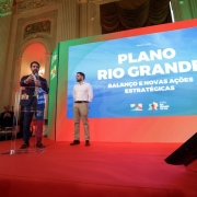 A foto mostra o governador Eduardo Leite e o vice-governador Gabriel Souza em um palco, com um tel&atilde;o ao fundo com as inscri&ccedil;&otilde;es "Plano Rio Grande: balan&ccedil;o e novas a&ccedil;&otilde;es estrat&eacute;gias". 